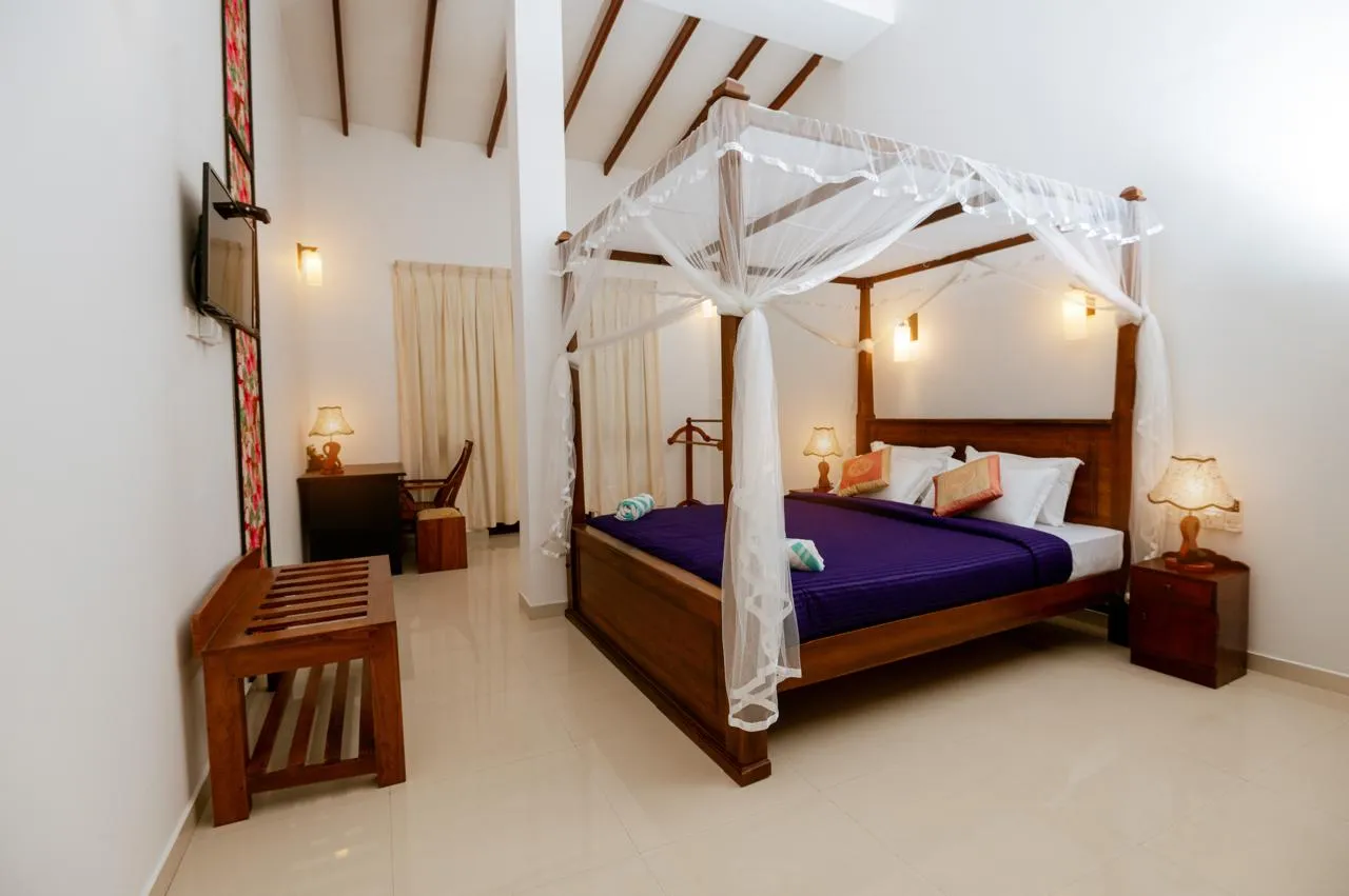 A wooden four-poster bed with white netting and purple bedding