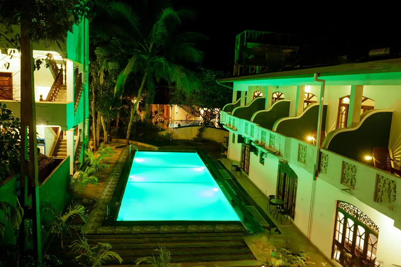 An illuminated swimming pool surrounded by palms and hotel balconies at night